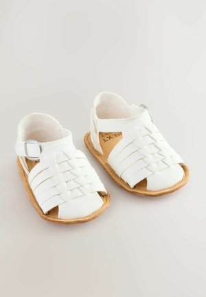Hvide lædersandaler med vævede stropper, justerbar spænde og korksål. Flad profil og åben tå design for åndbarhed.