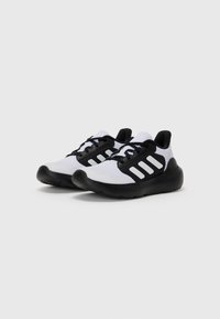 Chaussures de sport noir et blanc avec un dessus en mesh respirant et trois rayures horizontales sur le côté. Semelle texturée pour une meilleure adhérence.