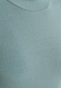 Närbild av ljusblå ribbad trikå med vertikal textur och en mjuk, rundad halsringning.