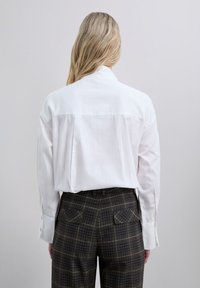 Camisa de algodón blanca con yugo trasero, combinada con pantalones de cuadro marrón que cuentan con bolsillos delanteros y traseros y una textura suave.