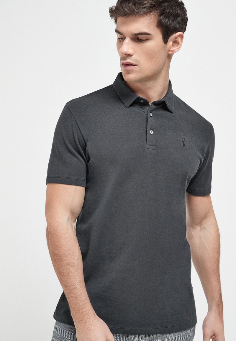 Dunkelgraues Polohemd mit einem kurzen Kragen, kurzer Knopfleiste mit drei Knöpfen und einem dezenten Logo auf der linken Brust. Hergestellt aus weichem Baumwollmaterial.