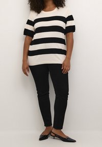 Zwart en crèmekleurig gestreept gebreid shirt met korte mouwen, gecombineerd met zwarte slimfit jeans en zwarte puntige slingback schoenen.