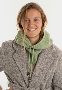 Grijze textuurcoat gelaagd over een geribde groene hoodie met trekkoorden en houten accenten. Lichte achtergrond benadrukt de kleding.