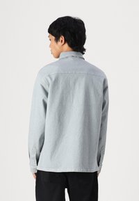 Lys grå denimskjorte med krage, lange ermer, knappeender og rett nederkant, brukt sammen med svarte bukser.