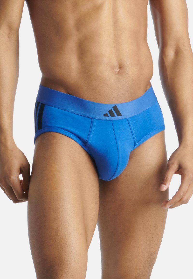 Un slip en coton bleu avec une ceinture élastique noire comportant trois bandes et un logo. Le design comprend une forme ajustée et une texture lisse.