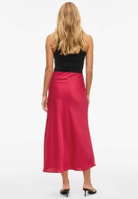 Rød sateng maxi-skjørt med en glatt tekstur, med en tettsittende midje og flytende design, kombinert med en svart tettsittende topp og sandaletter med hæl.