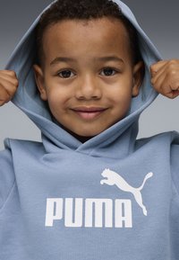 Sweatshirt azul claro feito de um tecido macio, com um grande logo branco "PUMA" e a silhueta de uma puma. O capô está ergido, mostrando um interior texturizado.