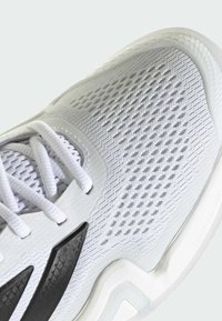 Biele športové topánky s sieťovinovým zvrškom, ktoré majú čierne akcenty a textúrované vzory. Šnúrkovanie, ľahká podrážka.