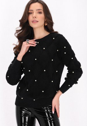 Zwarte donzige sweater met parelversieringen, diamantpatroon, ronde halslijn en geribde manchetten. G gedragen met glanzende zwarte broeken.