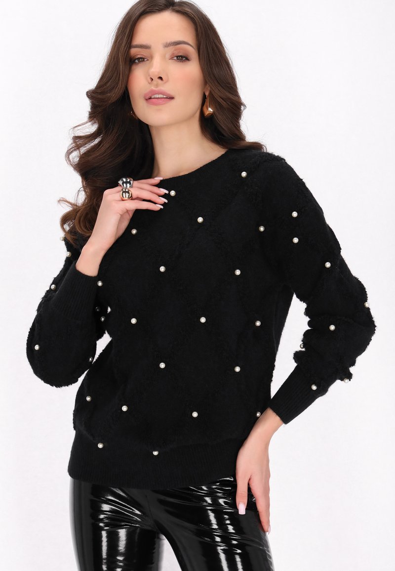 Schwarzer, flauschiger Pullover mit Perlenverzierungen, Rautenmuster, rundem Halsauschnitt und gerippten Bündchen. Getragen mit glänzenden schwarzen Hosen.
