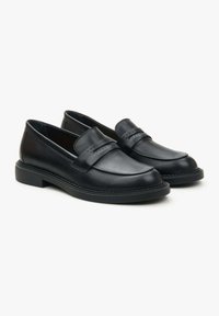 Zwarte leren loafers met een gladde afwerking, voorzien van een gebogen bovenkant, dubbele stiksel-details en een platte rubberen zool.