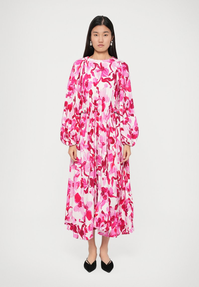 Rochie midi cu imprimeu floral în nuanțe de roz și alb, având mâneci lungi tip puff, talie strânsă și o siluetă fluidă. Pantofi plat cu vârful ascuțit, negri.
