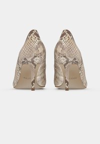 Chaussures à talons hauts beige avec un motif texturé en peau de serpent. Dotées d'une pointe effilée et d'un talon stiletto fin. Le logo de la marque est visible à l'intérieur.