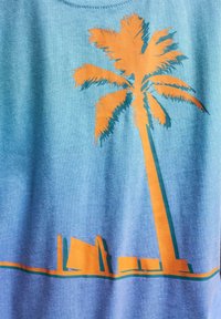 Bomull T-skjorte med et klart orange palme-tre grafikk mot en gradient blå bakgrunn, med nedre silhuetter i oransje og grønn.