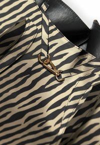 Sac fourre-tout en tissu beige avec des rayures zébrées noires, des détails en cuir et une fermeture à quincaillerie dorée. Surface texturée.