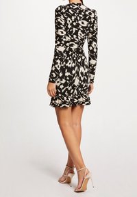 Czarna i biała sukienka mini w wzory z długimi rękawami, falbanastym dołem i dopasowaną talią, wykonana z teksturowanego materiału. Posiada wysoki dekolt.