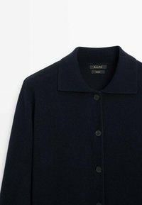 Granatowy kardigan z wełny z szerokim kołnierzem, długimi rękawami i sześcioma okrągłymi czarnymi guzikami z przodu. Miękka tekstura z minimalnymi detalami.