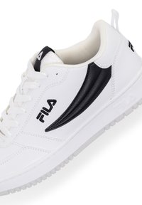 Sneaker bianco in pelle con dettagli neri, strisce laterali testurizzate, collarino imbottito e suola in gomma. Presenta il logo Fila in nero sul lato.