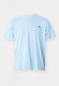 Camiseta de cuello redondo de manga corta en azul claro con un pequeño logotipo de cocodrilo verde en el lado izquierdo del pecho y un logotipo negro en la manga izquierda.