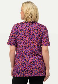 Černá tričko s krátkým rukávem s živým květinovým vzorem v purpurové, růžové a oranžové barvě. Materiál má hladkou texturu a uvolněný střih.
