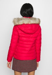 Czerwona kurtka puchowa z sztucznym futrem w kapturze, z pionowymi przeszyciami i kapturem ze sznurkiem, w połączeniu z spódnicą w kratę.