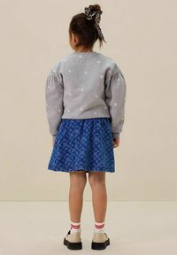 Sweat-shirt gris avec des fleurs blanches brodées, associé à une jupe bleue au motif floral. Chaussures noires avec des chaussettes rayées blanches et rouges.