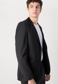 Črna jakna v obliki obleke z usklajeno zasnovo, notch reverjem in zapenjanjem na dva gumba. Narejena iz gladkega blaga z rahlo teksturo.