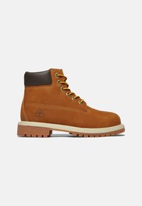 Stivale da trekking in suede beige con accenti in pelle marrone, lacci gialli e suola in gomma con un motivo di battistrada robusto. Logo Timberland sul lato.