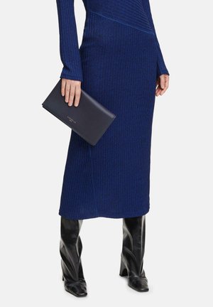 Robe en tricot bleu avec texture côtelée et manches longues, associée à des bottes noires élégantes jusqu'au genou et à un porte-monnaie noir.