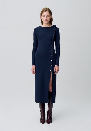 Robe à manches longues bleu marine avec une fente latérale, ornée de boutons dorés et d'un nœud sur l'épaule gauche. Texture de tissu lisse.