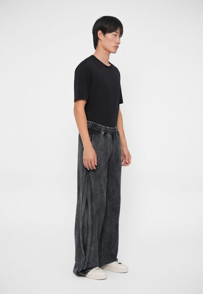 Schwarzes T-Shirt kombiniert mit weiten, dunkelgrauen Jeanshosen mit strukturiertem Finish und elastischem Bund. Weiße Sneakers runden das Outfit ab.