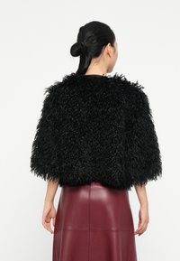 Veste en fourrure noire au design court et aux manches larges, associée à une jupe en simili cuir bordeaux. Le matériau texturé et duveteux crée un contraste saisissant.