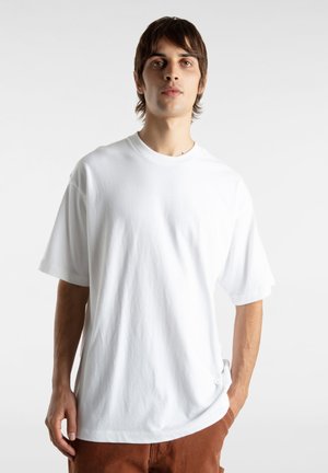 Witte katoenen T-shirt met een ronde hals, korte mouwen, een ontspannen pasvorm en een gladde textuur. G gedragen met roestkleurige broek. Eenvoudig ontwerp, geen patronen.