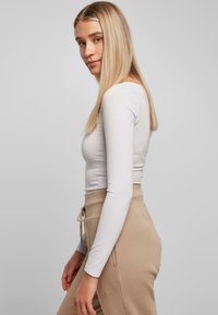 Hvit langermet, tettsittende topp kombinert med beige joggebukser med snøring; glatt tekstur, nøytrale farger og enkelt design.