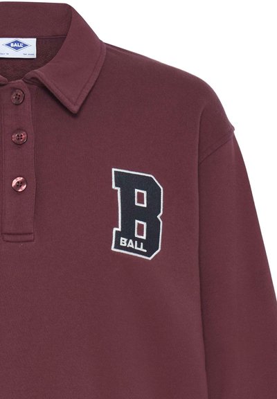 Burgundy színű póló, gallérral, három gombos lezárással, fekete hímzett "B" logóval, alatta a "BALL" felirattal. Sima pamut felület.