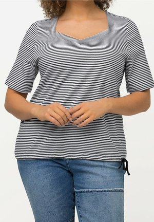 Vrouw draagt een zwart-wit gestreept kortermig shirt met een vierkante halslijn en blauwe jeans met een horizontale naad boven de knie.