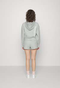 Sweatshirt cinza com capuz e detalhe gráfico nas costas, combinado com calções cinzentos semelhantes. O tecido tem uma textura suave. Ténis brancos e meias cor-de-rosa visíveis.