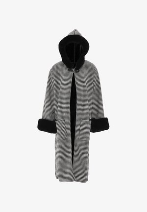 Kabát v černo-bílém houndstooth vzoru s kapucí, zdobený černým umělým kožešinovým lemem, se dvěma předními kapsami a volným střihem.