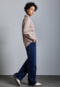 Camicia a maniche lunghe a righe beige chiaro abbinata a jeans a gamba larga blu scuro e sneakers bianche, che mostrano un fit rilassato e contemporaneo.