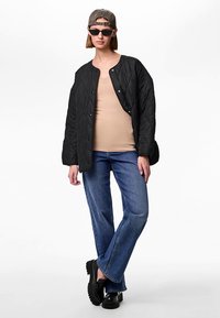 Fekete steppelt dzseki patentos gombokkal, bézs felső, szűkülő kék farmernadrág és fekete platform cipő. Kiegészítve napszemüveggel és sapkával.