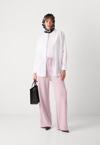 White button-up shirt, pink wide-leg trousers, black and white striped scarf, black handbag, and pointed black shoes. Smooth fabric textures.