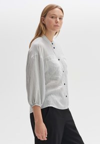 Light gray striped blouse with a mandarin collar, button-down front, two chest pockets, and gathered balloon sleeves, worn with black pants.