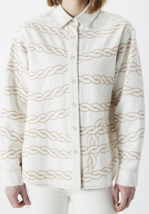 Biała koszula na guziki z beżowym wzorem łańcuszka noszona przez osobę, widoczny przedni tors i ramiona.