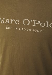 Oliven grøn bomuld t-shirt med hvid trykt tekst "Marc O'Polo EST. IN STOCKHOLM." Glat tekstur med rund halsudskæring.