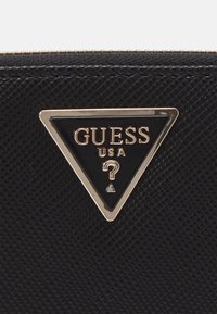 Black textured wallet featuring a triangular gold and black logo with "GUESS" and a question mark design. Smooth metallic accents included.