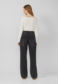 Jeans neri a gamba larga con vita alta, dotati di due tasche posteriori e una leggera sfumatura. Abbinati a una camicia a maniche lunghe di colore chiaro.