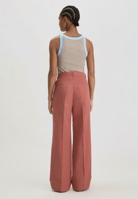 Bruin tanktop met blauwe afwerking, gecombineerd met high-waisted, wijde broek in een stoffige rozenkleur. De stof lijkt glad en textuurrijk.