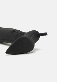 Black knee-high boot with a smooth fabric exterior, pointed toe, and a block heel. Features a side zipper and a sleek silhouette.