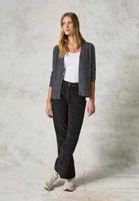 Grå cardigan över en vit topp, ihopparad med svarta kordflamsbyxor och vita sneakers. Slät textur, knappdetaljer och avslappnad passform.