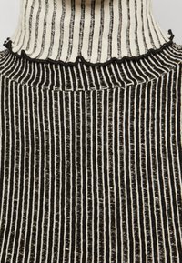 Maglione a collo alto a righe bianche e nere con una trama a coste. Presenta un bordo ondulato sul colletto e righe verticali uniformi su tutta la superficie.
